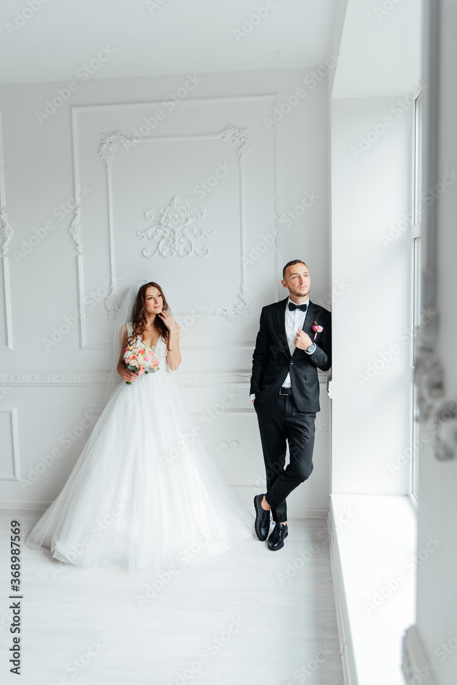 The first meeting of the groom in a black suit and the bride in a white wedding dress with a bouquet in the interior of a photo studio on a white and black background The first meeting of the groom in a black suit and the bride in a white wedding dress with a bouquet in the interior of a photo studio on a white and black background