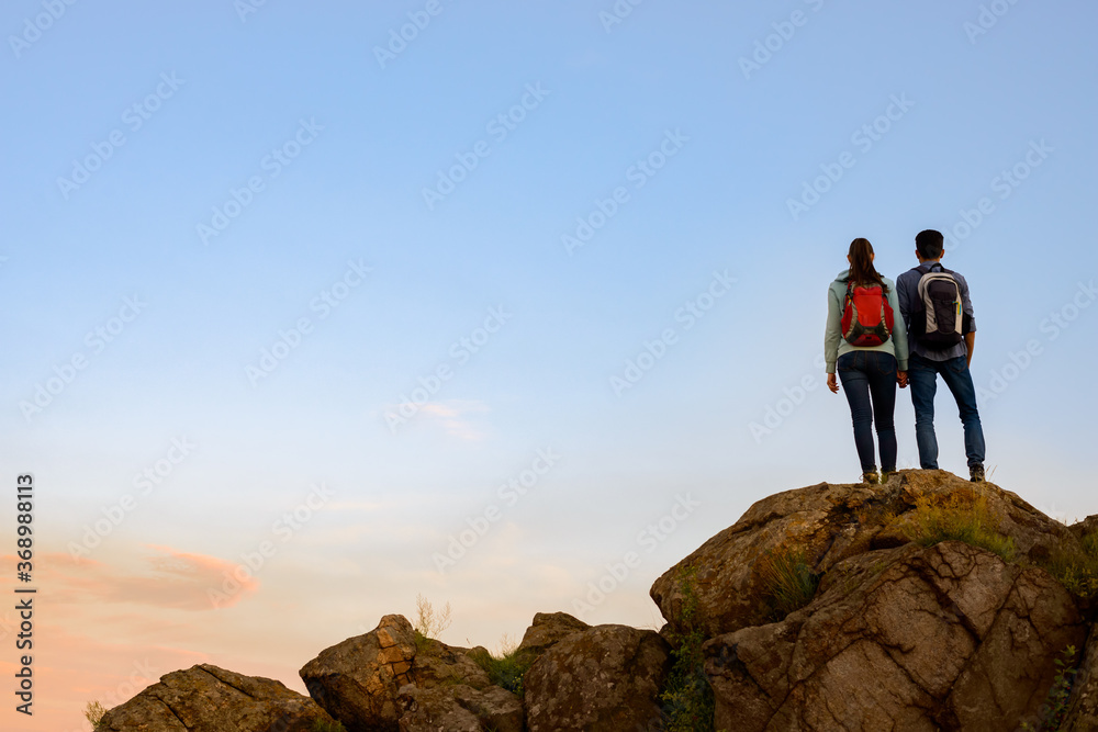Couple of Young Travelers Standing on the Top of the Rock at Summer Sunset. Family Travel and Adventure Concept