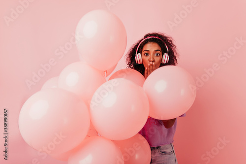 Wallpaper Mural Surprised african girl in headphones hiding behind balloons. Funny black lady having fun at birthday party. Torontodigital.ca
