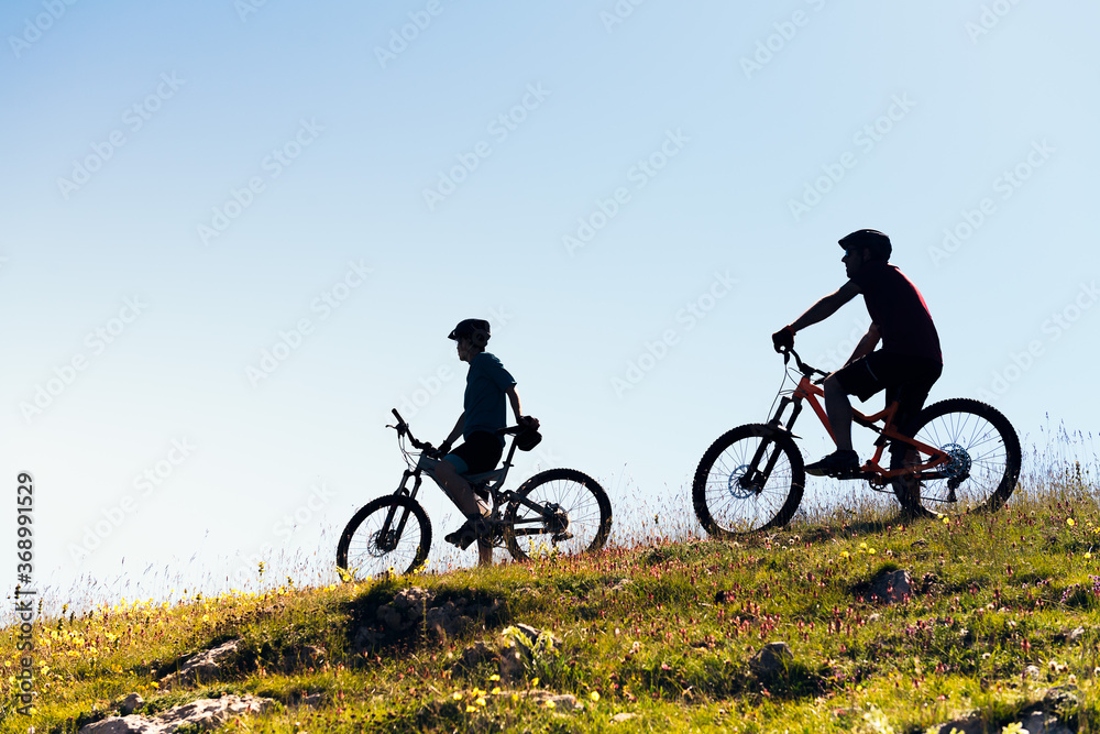 silhouette of two young men with mountain bikes