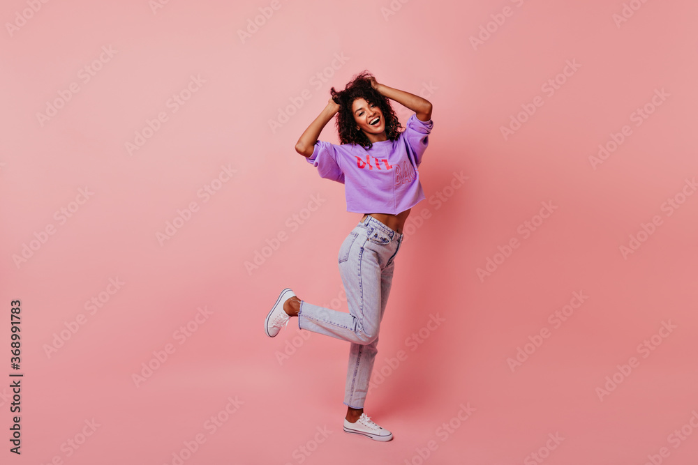 Full-length portrait of optimistic laughing woman dancing in studio. Relaxed curly female model enjoying life.