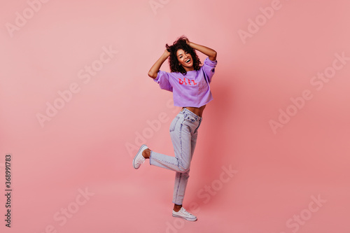Full-length portrait of optimistic laughing woman dancing in studio. Relaxed curly female model enjoying life. © Look!
