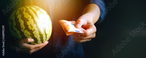 Costumer holding fresh watermelon and the other hand send the money. Buying or selling fresh farmer organic fruit for summer season.