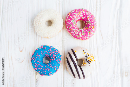 Top view of four tasty colorful donuts on a white wooden background. Sweet and colorful donuts. Dessert. Homemade sweets. Café dessert for birthday or party, top view, with copy space