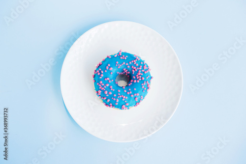 Top view of tasty blue colored donut on a small white plate with blue background. Sweet and colorful donuts. Dessert. Homemade sweets. Café dessert for birthday or party, top view, with copy space