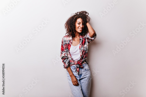 Slim black girl in trendy outfit posing with enjoyment in studio. African short-haired lady standing on white background.