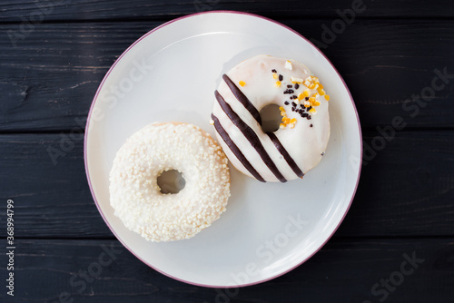 Two assorted donuts on a small white plate with black background. Fresh sweet colorful homemade vanilla donuts on vintage background for birthday or party, top view, with free space for text