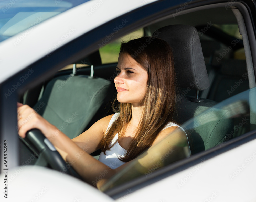 Positive young adult woman driving car during solo trip, side view