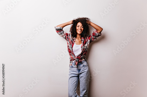 Slim amazing african girl expressing positive emotions on white background. Indoor photo of debonair laughing woman with short curly hair posing in checkered shirt.
