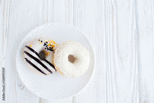 Top view of two donuts on a small white plate with white background. Fresh sweet colorful homemade vanilla donuts on vintage background for birthday or party, with free space for text