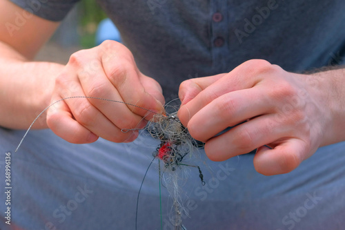 Man untangles a fishing line and hooks preparing to fishing, hands closeup. Fishing equipment and tools for catching fish. photo