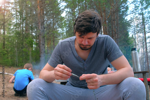 Man untangles a fishing line and hooks preparing to fishing on nature. Fishing equipment and tools for catching fish. Family forest camping, resting outdoors. photo