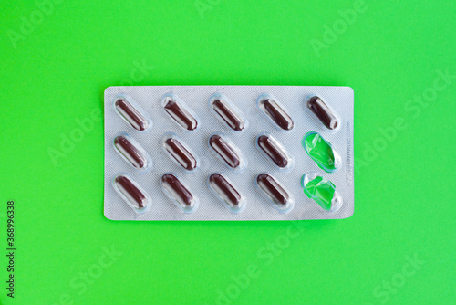 Pills isolated on a bright green background. Pack of brown pills and capsule packs. Set of tablets in capsules. A kit of medical pills for treatment. Pharmaceutical blister pack