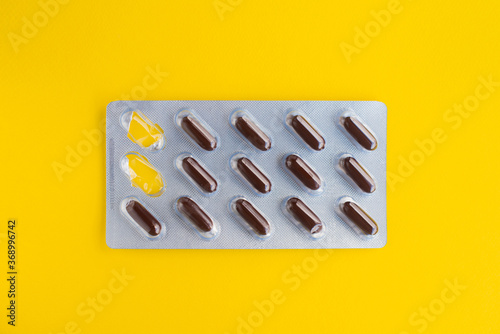 Pills isolated on a bright yellow background. Pack of brown pills and capsule packs. Set of tablets in capsules. A kit of medical pills for treatment. Pharmaceutical blister pack