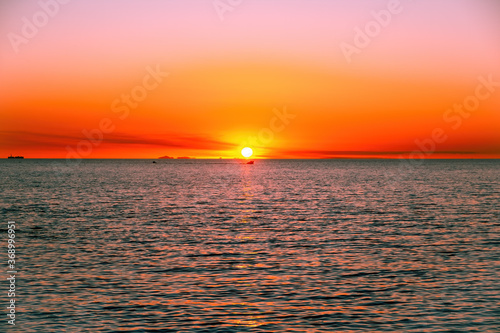 Vivid red glowing sunset over sea with small fishing boat - minimalist seascape with copy space