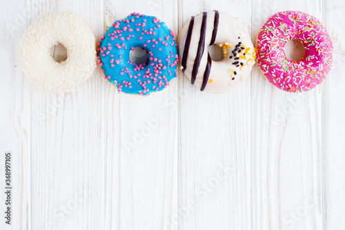 Row of four tasty colorful donuts on a white wooden vintage background. Sweet and colorful donuts. Dessert. Homemade sweets. Café dessert for birthday or party, top view, with copy space