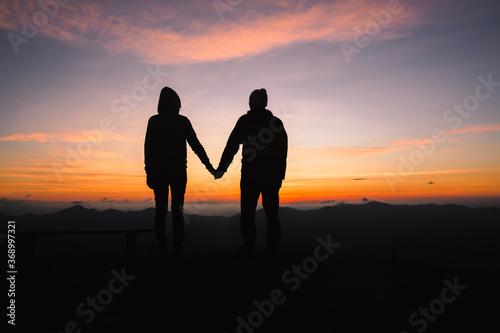 silhouette of a man and woman holding hands with each other  with a beautiful sunset in background.  happy lifestyle concept. © Tinnakorn