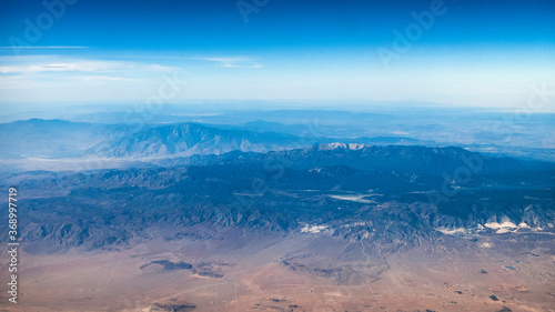 Beautiful mountains and valleys of the desert American southwest with red, blue and green scenery viewed from the airplane with white puffy clouds