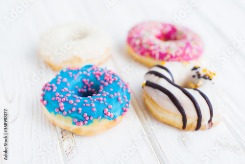 Top view of four tasty colorful donuts on a white wooden vintage background. Sweet and colorful donuts. Dessert. Homemade sweets. Café dessert for birthday or party, top view, with copy space