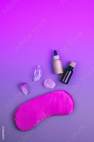 Top view of gemstones crystal minerals, pink eye pillow, glass and wooden bottles for essential oils over neon colored background. Place for text. Relaxation and meditation concept.