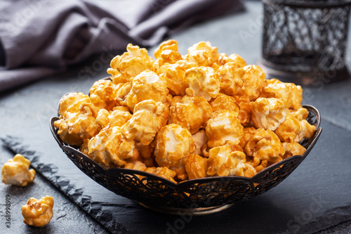 Popcorn in caramel glaze in a plate on a dark concrete table. Copy space. photo