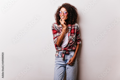 Gorgeous black female model in vintage jeans smiling to camera. Studio portrait of playful african lady wears red checkered shirt.