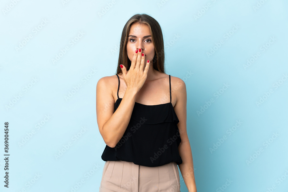 Young Uruguayan woman isolated on blue background covering mouth with hand Young Uruguayan woman isolated on blue background covering mouth with hand