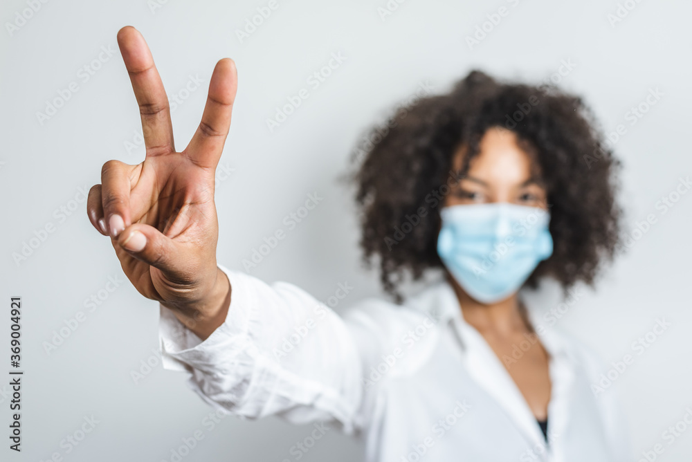 hand of an afro young woman using a surgical mask and making victory symbol with fingers hand of an afro young woman using a surgical mask and making victory symbol with fingers
