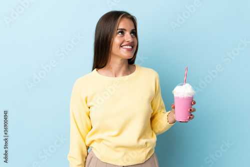 Young Uruguayan woman with strawberry milkshake isolated on blue background thinking an idea while looking up