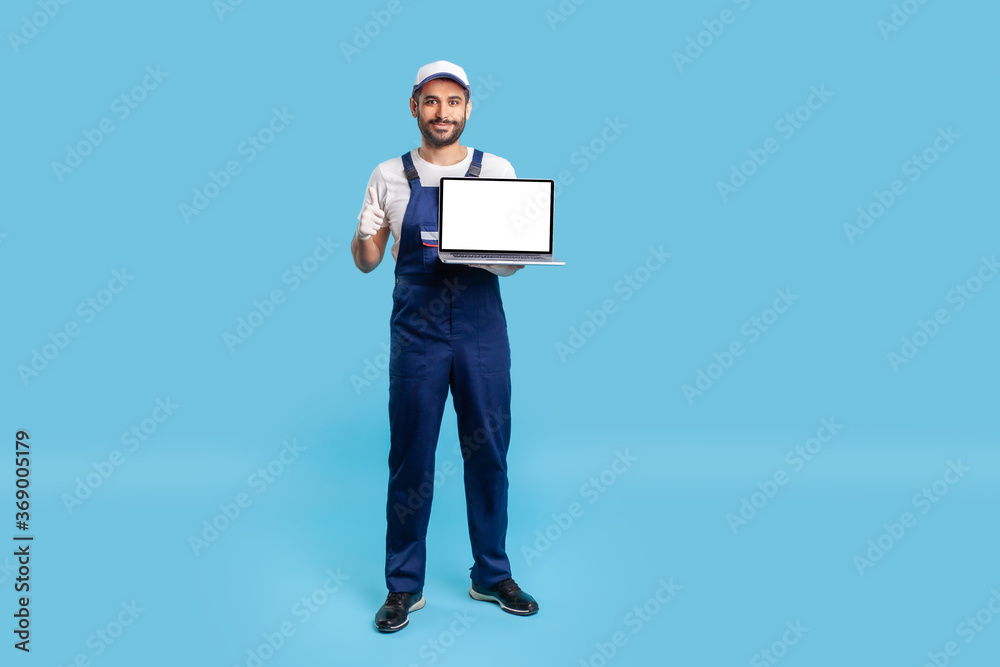 Full length high-qualified worker man in uniform showing thumbs up and holding laptop with mock up blank display, empty space for advertise, message or repair service order. studio shot isolated Full length high-qualified worker man in uniform showing thumbs up and holding laptop with mock up blank display, empty space for advertise, message or repair service order. studio shot isolated
