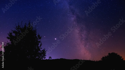 Space background. A hill with a tree against the backdrop of a milky way of millions of stars.