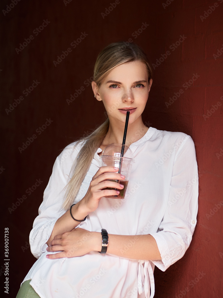 Outdoor summer city lifestyle portrait of young trendy dressed blonde happy woman with lemonade drink having fun outdoor in the city ready for travel