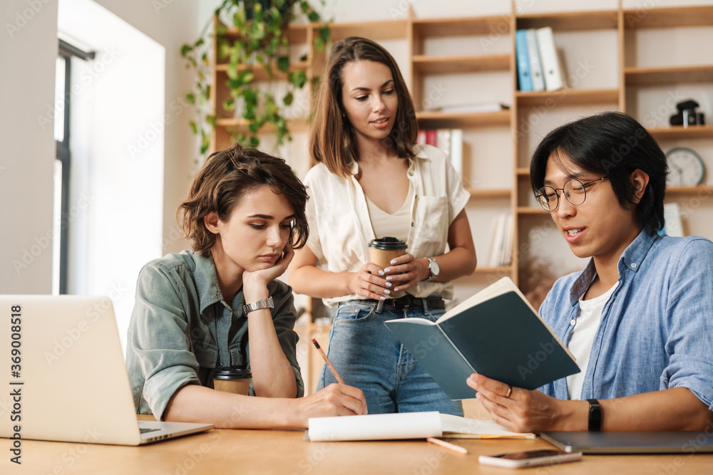 Image of young colleagues discussing project and drinking coffee