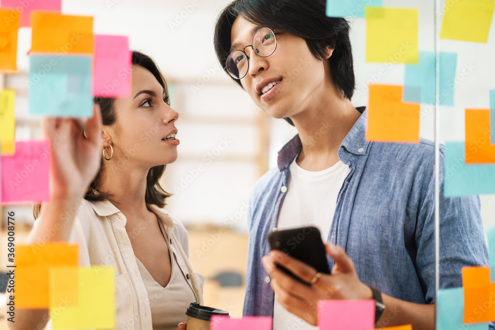 Image of multinational pleased colleagues using mobile phone and talking Image of multinational pleased colleagues using mobile phone and talking