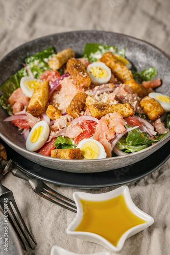 Close-up Caesar salad with red fish, romaine lettuce, quail eggs, garlic croutons and olive oil. Vertical shot