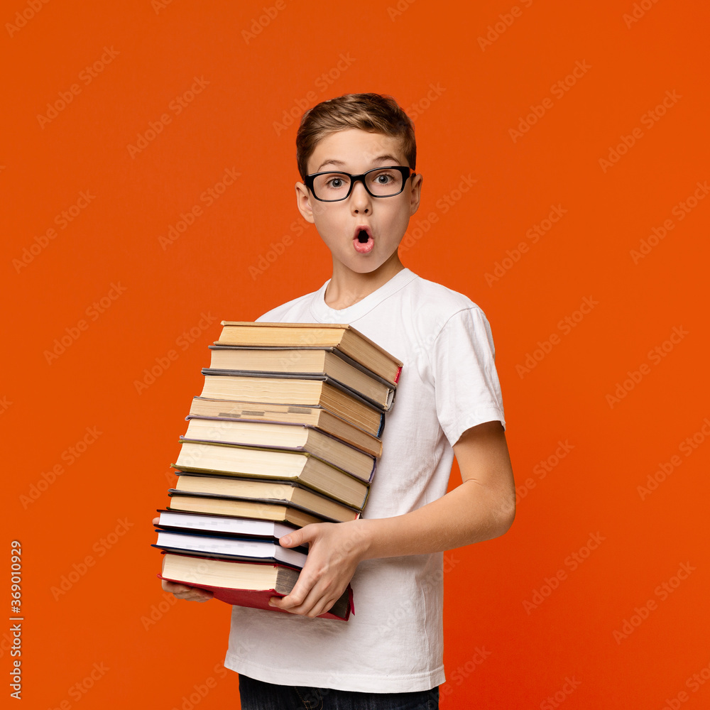 Shocked schoolboy in glasses holding stack of books Shocked schoolboy in glasses holding stack of books
