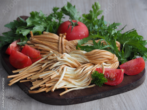 Smoked braided cheese pigtail, fresh spicy herbs, tomatoes on the kitchen wooden board closeup. Traditional salty string cheese with gourmet vegetables
