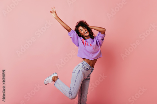 Fototapeta Naklejka Na Ścianę i Meble -  Shapely jocund girl dancing on rosy background. Good-humoured african lady jumping with smile.