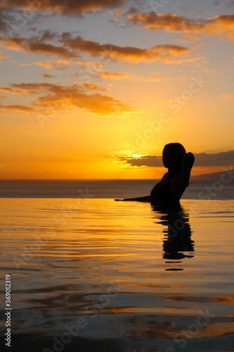  a Girl is standing in the pool, supporting her hair with her hand, against the background of a beautiful sunset. hotel Las Terrazas de Abama