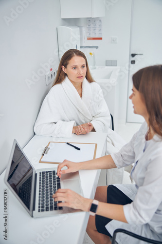 Young woman patient feeling confused while talking with cosmetologist