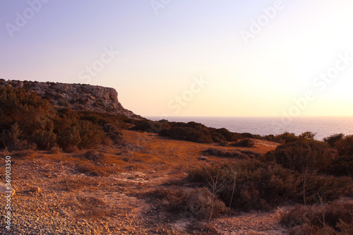 View from below on the red stony soil and Cape Cavo Greco (Capo Greco) in the sunset. Cyprus.