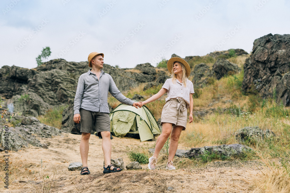 Happy young couple travelers in casual outfits with tent on the mountain background. Local