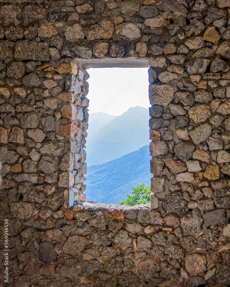 view to distant mountains from old window frame on rough stone wall