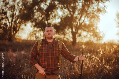 Irish looking red bearded hunter in checkered shirt staying outdoors in the sunset light and holding his gun © honey_inside