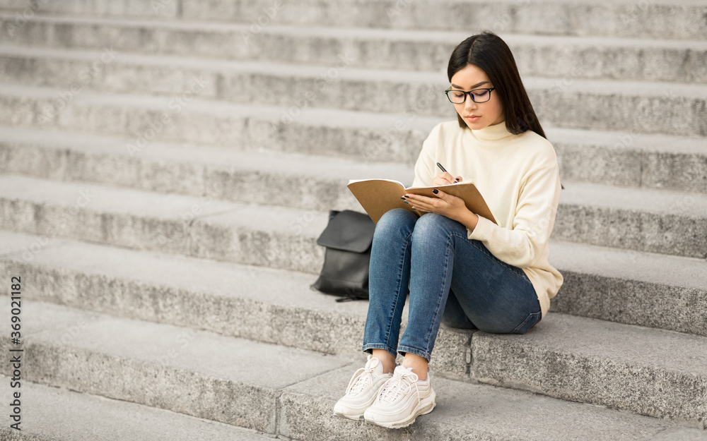 Girl writing in her diary, sitting on the gray stairs