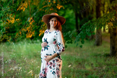a pregnant woman in a dress and hat walks in the forest in summer, a pregnant girl's walk in nature