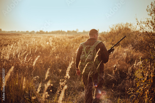 Papier peint Young hunter in the sunny field with military backpack and shotgun waiting for f