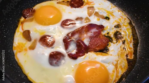 Delicious hearty breakfast. Egg omelette while frying with smoked sausage rings and ham slice. Cooking in non-stick black stone pan.