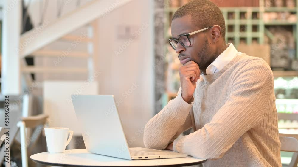 Pensive African Man Thinking and Working on Laptop in Cafe