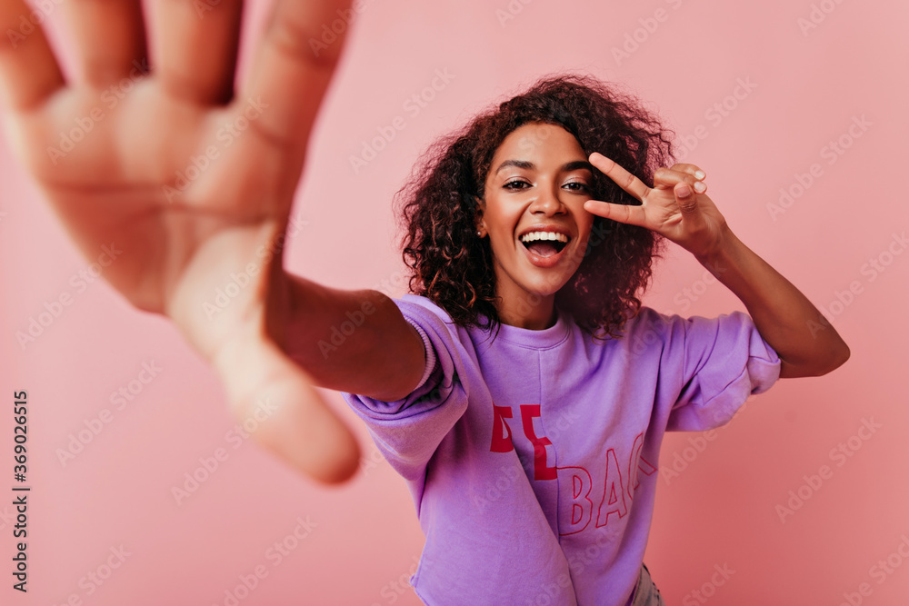 Blithesome black woman with wavy hair making selfie on rosy background. Wonderful girl with positive smile taking picture of herself. Blithesome black woman with wavy hair making selfie on rosy background. Wonderful girl with positive smile taking picture of herself.